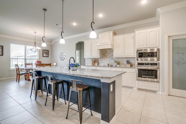 kitchen featuring white cabinetry, stainless steel appliances, light stone counters, and a center island with sink