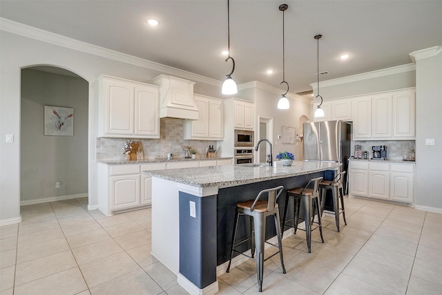 kitchen featuring white cabinetry, light stone counters, light tile patterned floors, an island with sink, and custom range hood