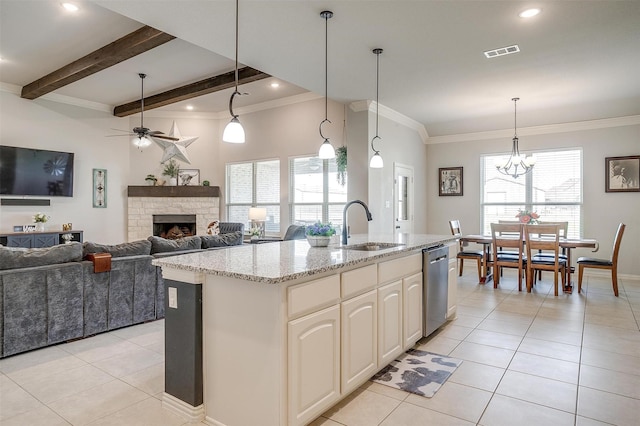 kitchen featuring a stone fireplace, decorative light fixtures, a kitchen island with sink, stainless steel dishwasher, and light stone counters