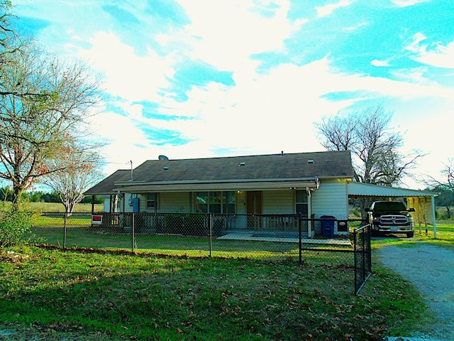 back of house featuring dirt driveway, a carport, a fenced front yard, and a lawn