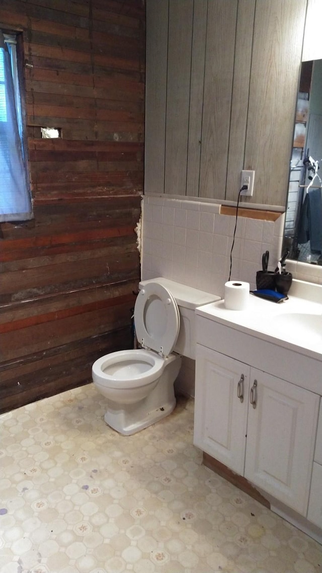 half bathroom with vanity, wooden walls, decorative backsplash, tile patterned floors, and toilet