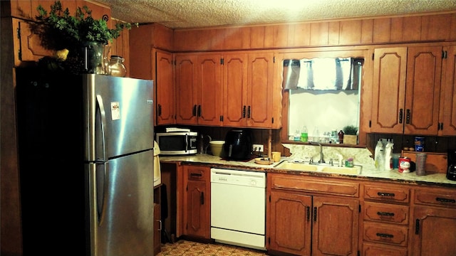 kitchen with a sink, a textured ceiling, brown cabinets, and stainless steel appliances