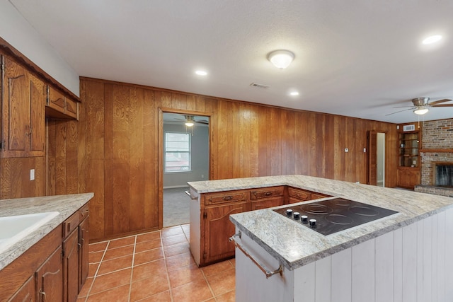 kitchen with light tile patterned flooring, a fireplace, a center island, ceiling fan, and black electric cooktop