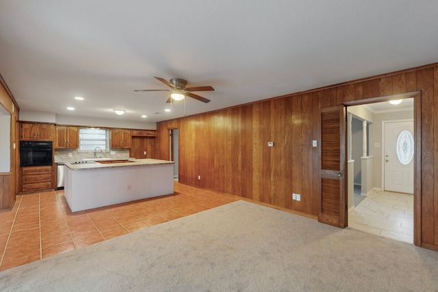 kitchen featuring light colored carpet, wooden walls, black oven, ceiling fan, and backsplash