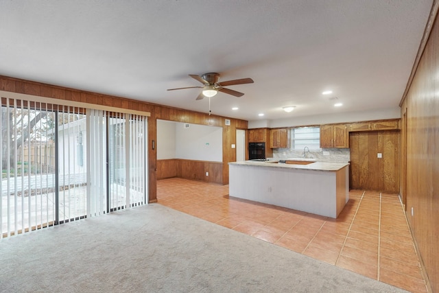 kitchen with sink, ceiling fan, wooden walls, light carpet, and kitchen peninsula