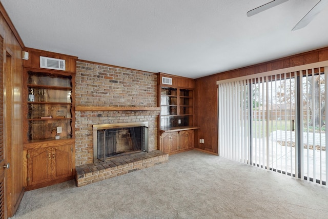 unfurnished living room featuring built in shelves, light colored carpet, wooden walls, and a brick fireplace