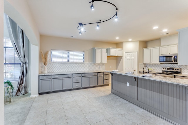 kitchen featuring appliances with stainless steel finishes, sink, backsplash, light tile patterned flooring, and light stone countertops