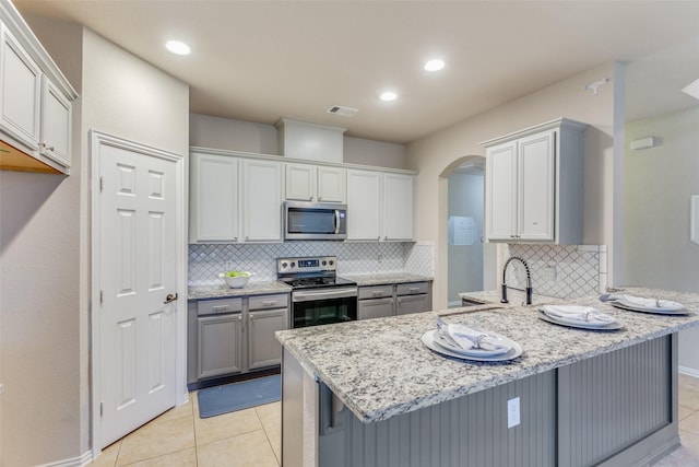 kitchen featuring gray cabinetry, a breakfast bar area, stainless steel appliances, light tile patterned floors, and kitchen peninsula