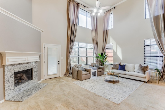 carpeted living room featuring ceiling fan, a towering ceiling, a wealth of natural light, and a premium fireplace