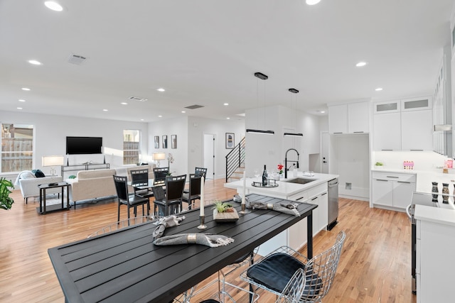 kitchen featuring pendant lighting, sink, white cabinets, light hardwood / wood-style floors, and stainless steel appliances