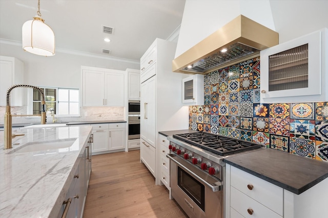 kitchen featuring sink, designer range, custom range hood, white cabinets, and dark stone counters