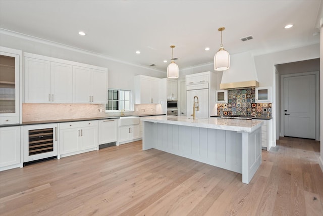 kitchen featuring white cabinetry, beverage cooler, custom exhaust hood, hanging light fixtures, and paneled built in fridge