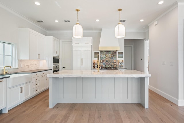 kitchen with custom exhaust hood, hanging light fixtures, a center island with sink, and paneled built in fridge