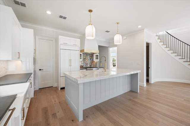 kitchen featuring a large island with sink, white cabinets, paneled built in fridge, and decorative light fixtures