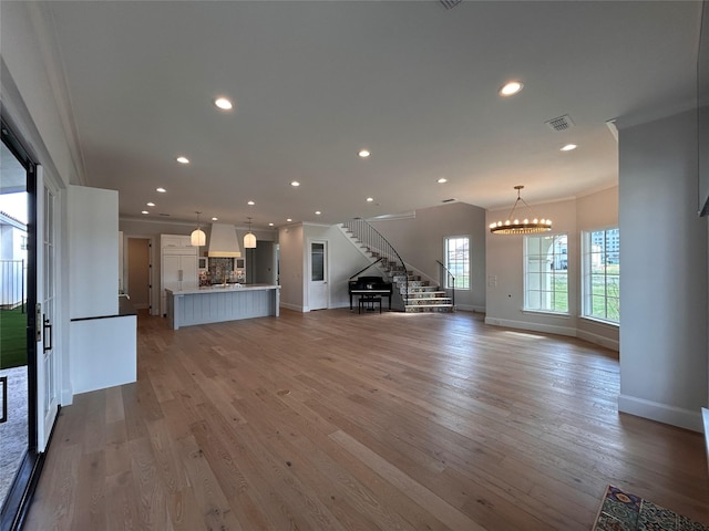 unfurnished living room featuring ornamental molding, a notable chandelier, and light hardwood / wood-style floors