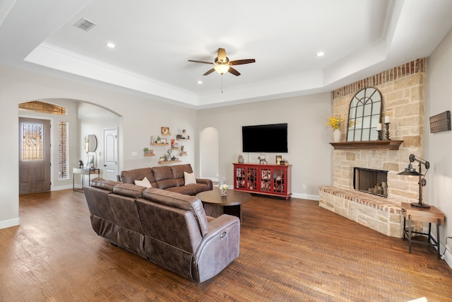 living room featuring ceiling fan, a fireplace, a tray ceiling, and dark hardwood / wood-style flooring