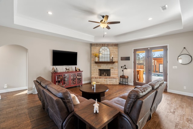 living room with a fireplace, hardwood / wood-style flooring, ceiling fan, a raised ceiling, and french doors