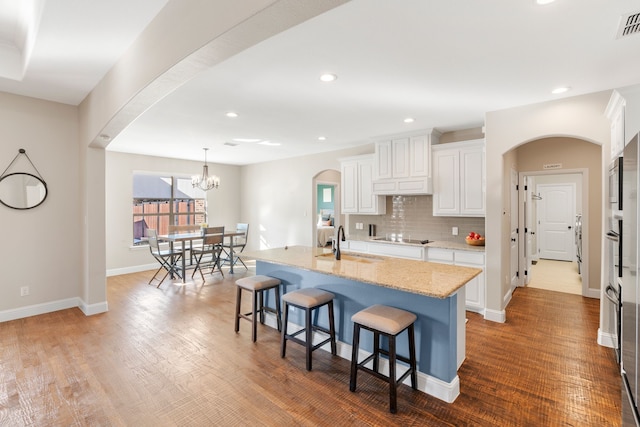 kitchen with an island with sink, sink, white cabinets, hanging light fixtures, and light stone countertops