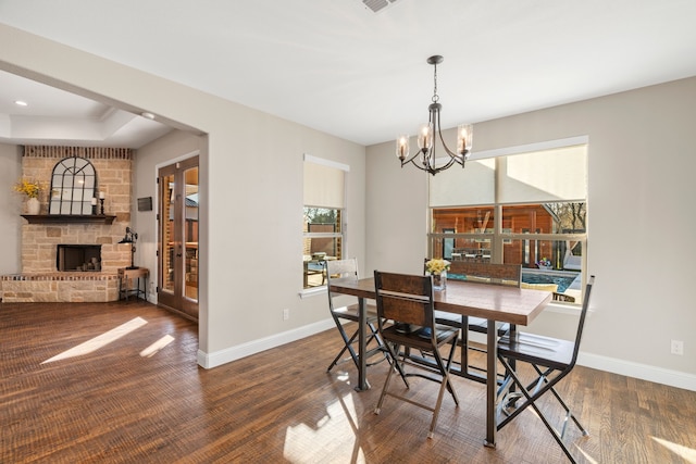 dining room with a notable chandelier, a stone fireplace, and dark wood-type flooring