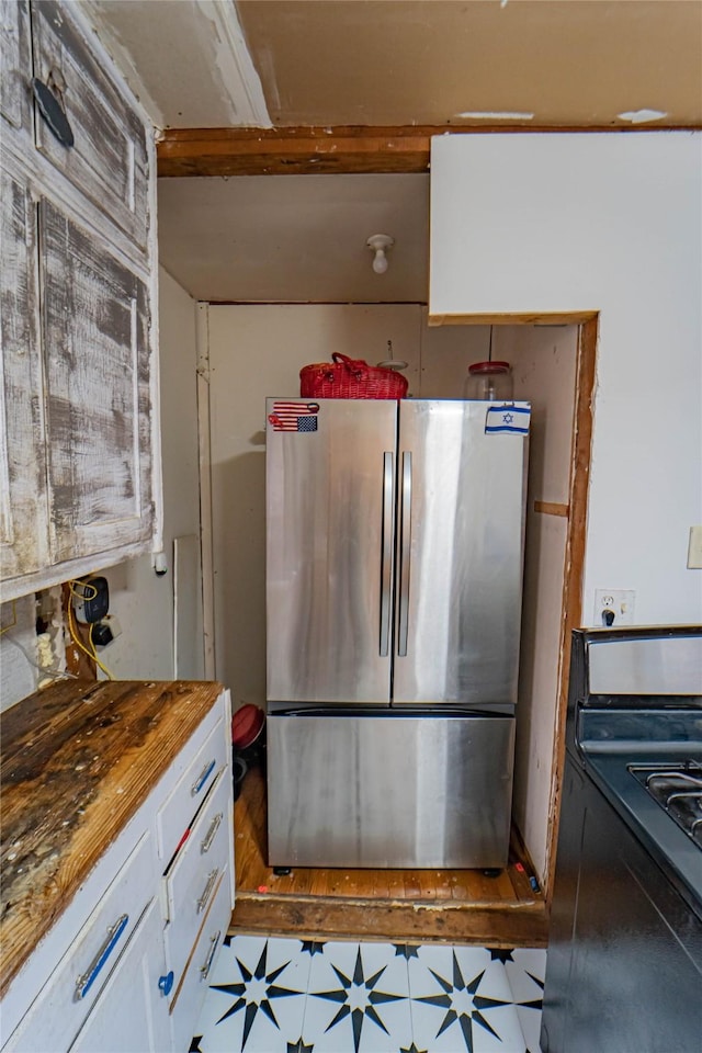 kitchen featuring stove, wood counters, stainless steel refrigerator, and white cabinets