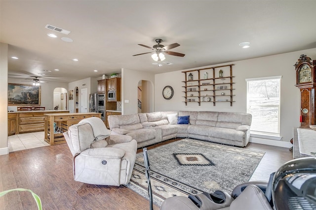 living room featuring ceiling fan, visible vents, arched walkways, and light wood-style flooring