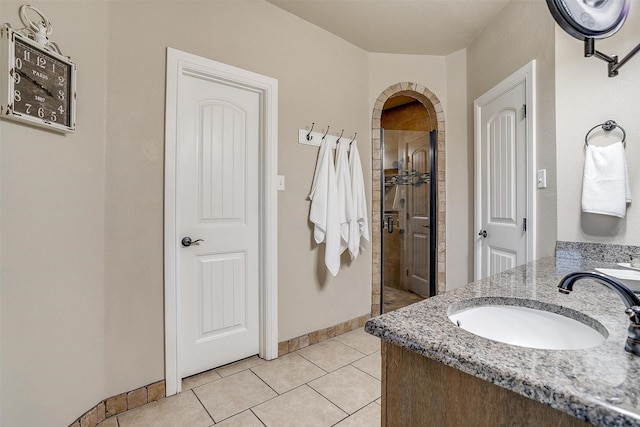 full bath featuring baseboards, double vanity, a sink, a shower stall, and tile patterned floors