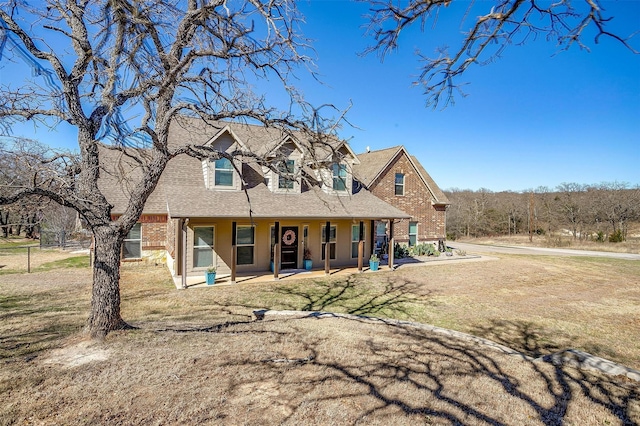 view of front of home with brick siding, a shingled roof, a front lawn, fence, and covered porch