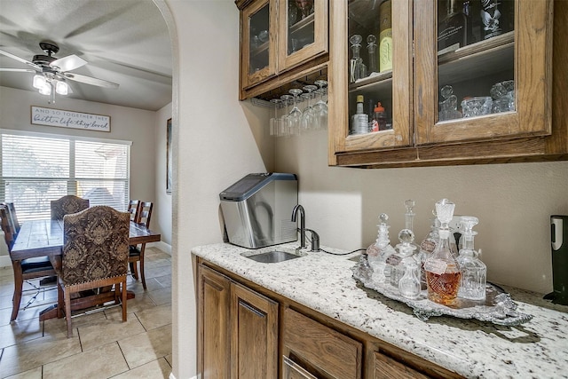 kitchen with a sink, arched walkways, brown cabinets, and light stone countertops