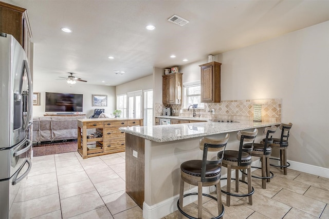 kitchen featuring visible vents, a peninsula, decorative backsplash, stainless steel refrigerator with ice dispenser, and open floor plan