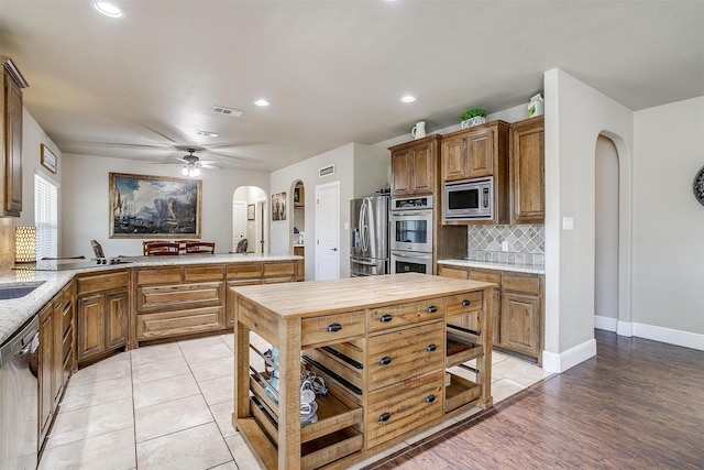 kitchen featuring a peninsula, arched walkways, ceiling fan, stainless steel appliances, and backsplash