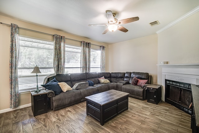 living area with crown molding, a fireplace, visible vents, light wood-style flooring, and ceiling fan