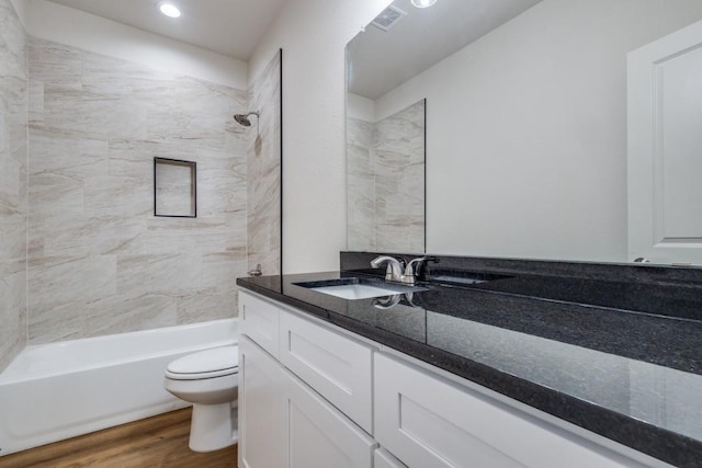 full bathroom featuring hardwood / wood-style flooring, tiled shower / bath, vanity, and toilet