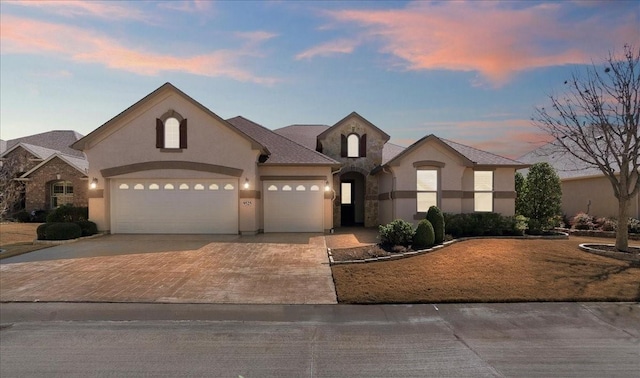 french country inspired facade featuring concrete driveway, an attached garage, and stucco siding