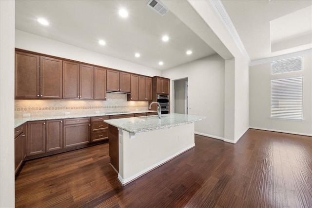 kitchen featuring dark wood-style floors, a center island with sink, black electric stovetop, visible vents, and a sink