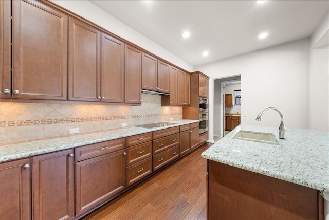 kitchen featuring black electric cooktop, a sink, light stone countertops, dark wood-style floors, and tasteful backsplash