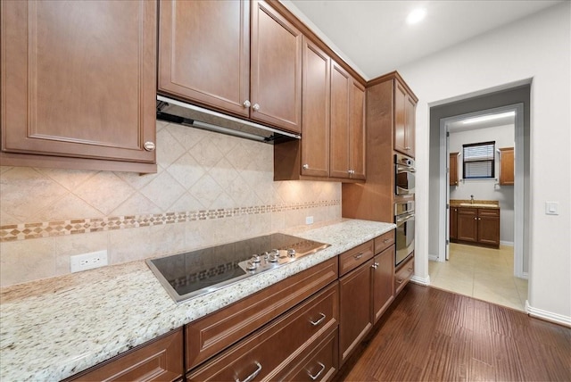 kitchen featuring baseboards, dark wood-style flooring, black electric cooktop, under cabinet range hood, and backsplash