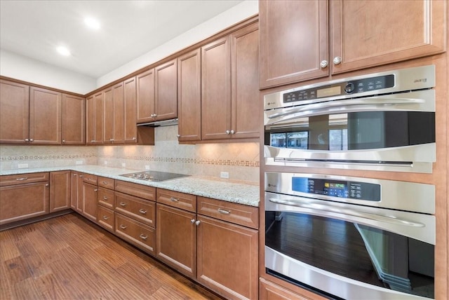 kitchen featuring light stone counters, decorative backsplash, dark wood-type flooring, under cabinet range hood, and black electric cooktop