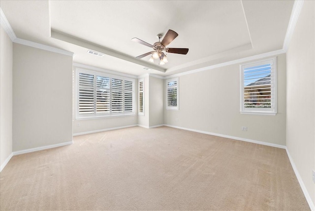 spare room with ceiling fan, visible vents, baseboards, a tray ceiling, and crown molding