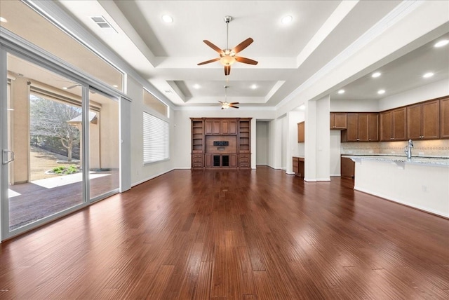 unfurnished living room with a tray ceiling, dark wood-style flooring, a fireplace, visible vents, and baseboards