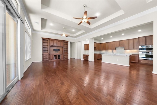 unfurnished living room featuring a fireplace, a tray ceiling, dark wood-style flooring, and ornamental molding