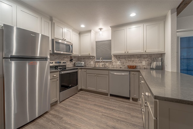 kitchen with sink, a textured ceiling, light hardwood / wood-style flooring, appliances with stainless steel finishes, and backsplash