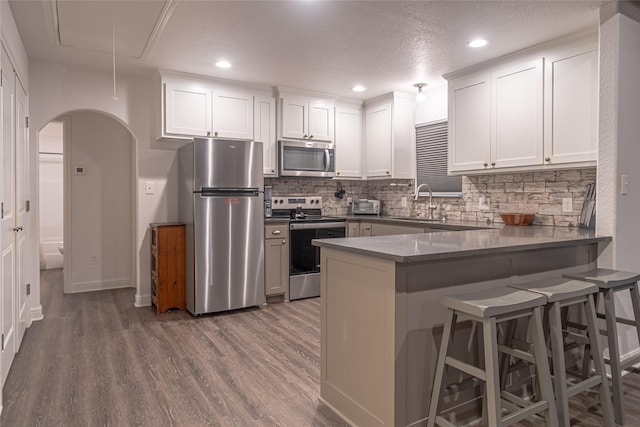 kitchen featuring a breakfast bar area, white cabinetry, tasteful backsplash, kitchen peninsula, and stainless steel appliances