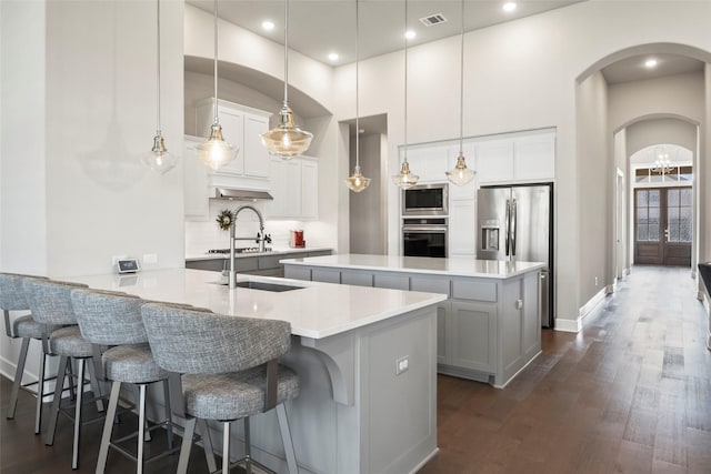 kitchen featuring white cabinetry, decorative light fixtures, dark hardwood / wood-style flooring, stainless steel appliances, and a kitchen island with sink