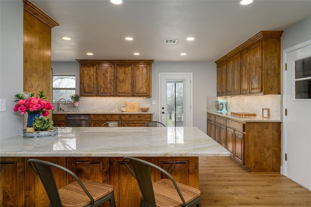 kitchen with sink, light stone counters, tasteful backsplash, light hardwood / wood-style flooring, and kitchen peninsula