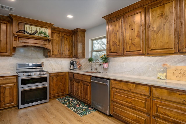 kitchen with sink, light hardwood / wood-style flooring, premium range hood, appliances with stainless steel finishes, and decorative backsplash