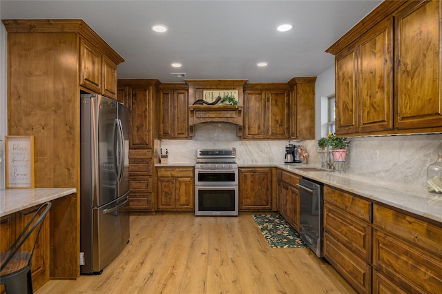 kitchen featuring appliances with stainless steel finishes, sink, light stone counters, custom range hood, and light hardwood / wood-style flooring