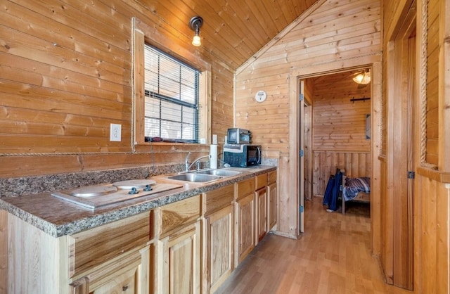 kitchen with vaulted ceiling, wooden walls, sink, light brown cabinets, and light wood-type flooring