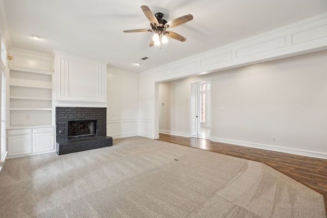 unfurnished living room featuring built in shelves, ceiling fan, ornamental molding, and a brick fireplace