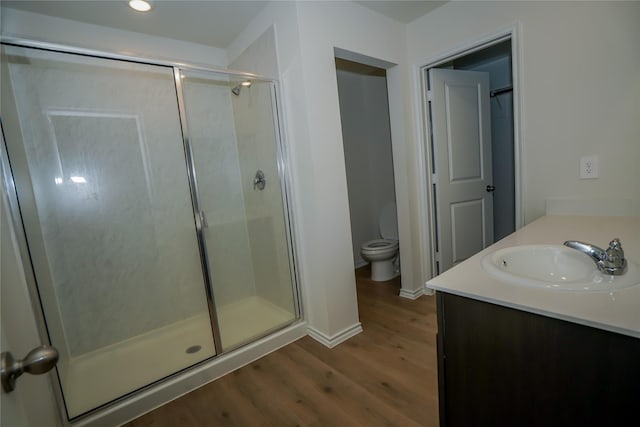 bathroom featuring toilet, vanity, a shower with shower door, and wood-type flooring