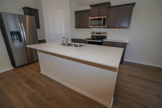 kitchen with a center island with sink, stainless steel appliances, dark brown cabinetry, dark hardwood / wood-style flooring, and sink